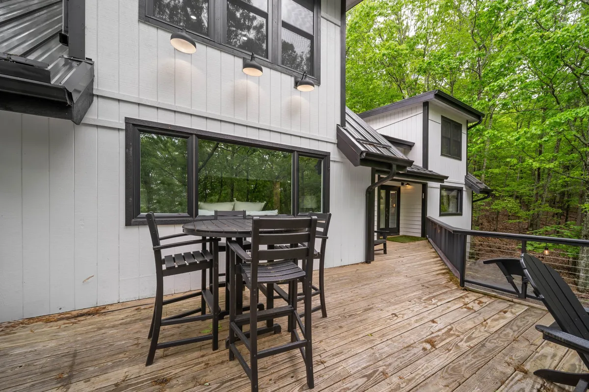 This image showcases a spacious wooden deck surrounded by lush greenery, featuring an outdoor dining set. The space is inviting and designed for relaxation or gathering, with views into the trees and an open sky above, perfect for capturing the changing seasons.