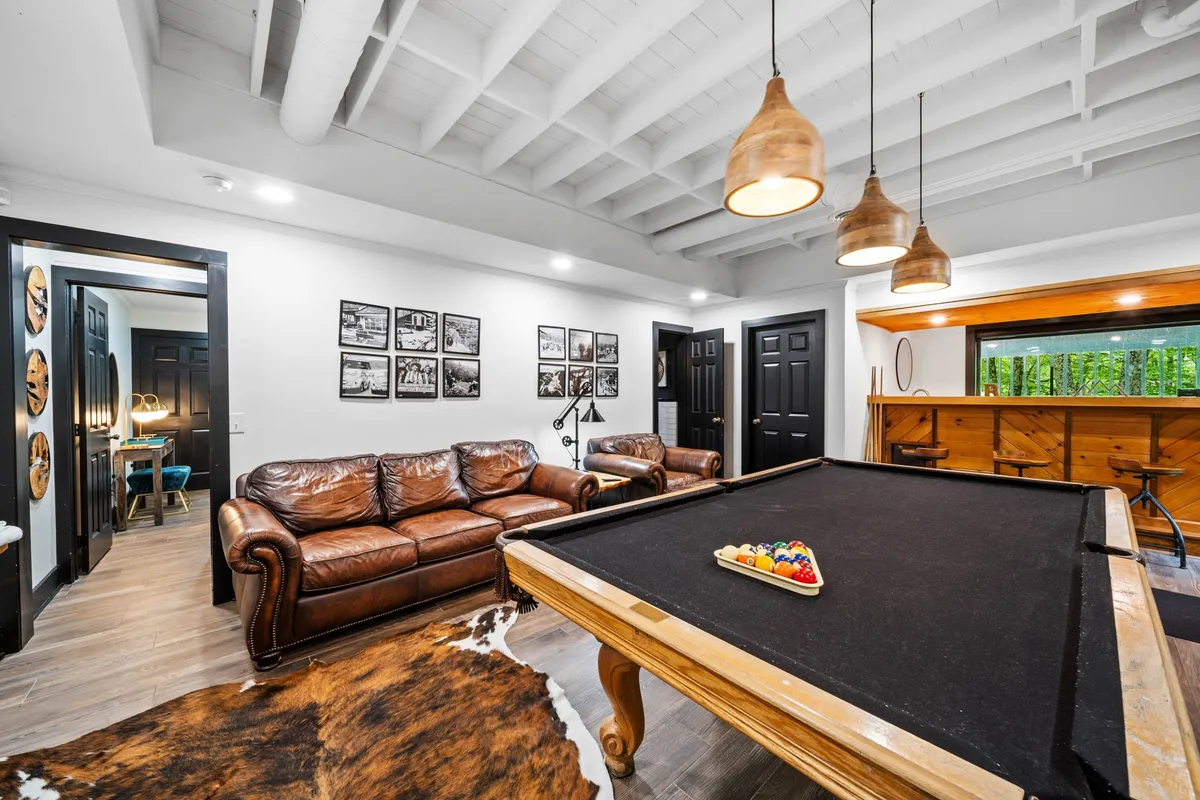 A cozy entertainment area with a pool table, plush brown leather sofas, and a rustic wooden bar area, accented by wall-mounted photographs. The space invites both competitive play and relaxed conversation after a day exploring the mountains.