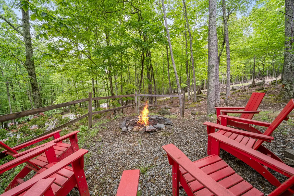 A cozy fire pit encircled by vibrant red chairs, set against a backdrop of green trees. The arrangement is intimate, suggesting evenings of conversation, stargazing, and relaxation in a tranquil mountain environment.
