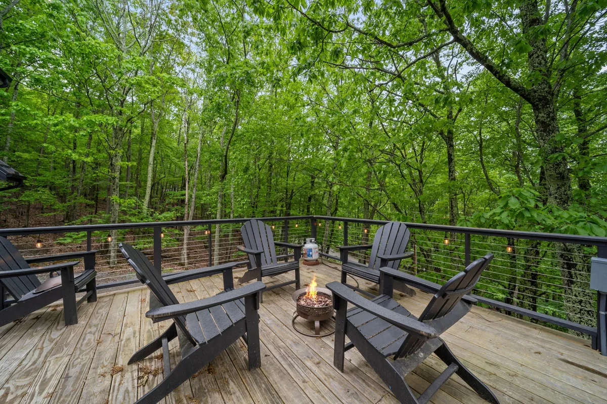 A cozy firepit scene with wooden chairs arranged in a circle, nestled among towering trees. The setting is ideal for gathering, sharing stories, or enjoying an evening under the stars.