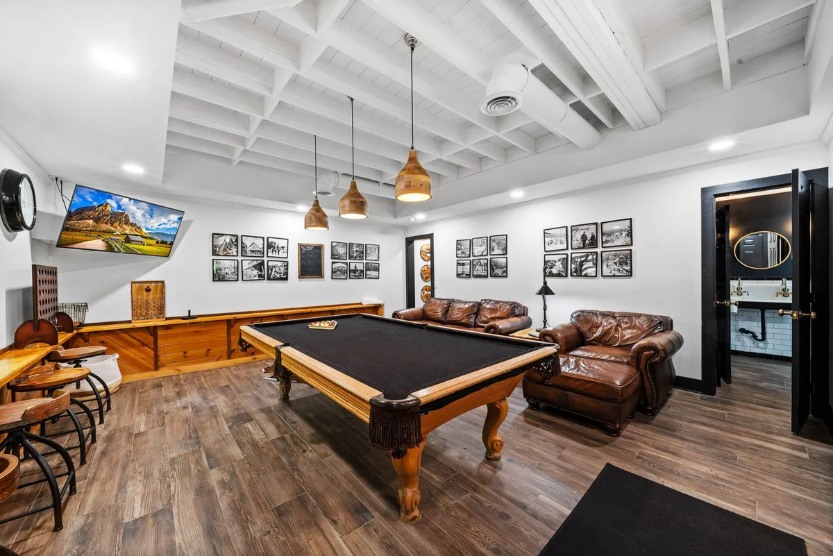 A stylish game room featuring a pool table at the center, surrounded by comfortable leather sofas and modern wall art. The room exudes a casual, welcoming vibe, perfect for unwinding after outdoor adventures with friends or family.
