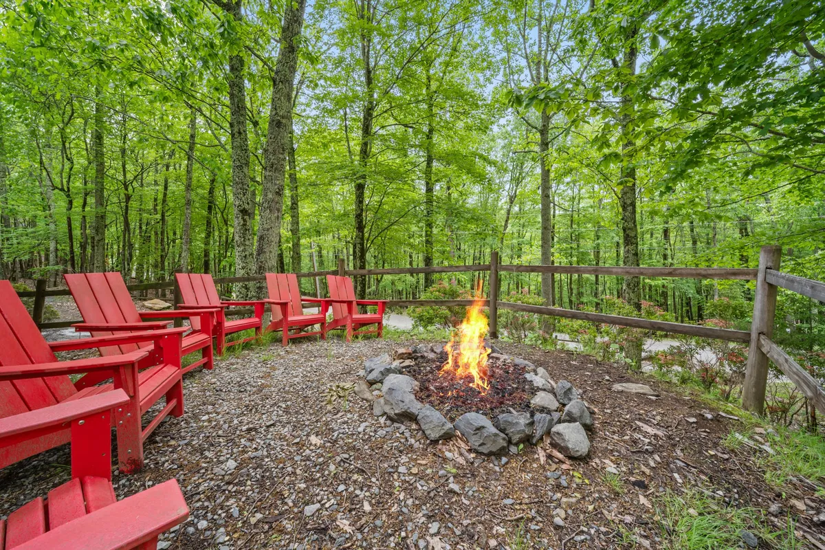 Featuring a cozy fire pit encircled by red chairs amidst lush trees, this exterior scene captures families or friends gathering outside. The setting is ideal for storytelling, making s’mores, and enjoying evenings under the stars.
