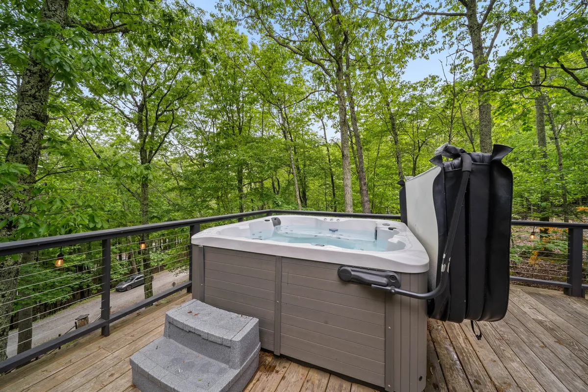 This exterior image showcases the Beech House’s expansive deck surrounded by towering trees, with a hot tub invitingly set for relaxation. The sunset sky casts a warm glow, while the deck’s spaciousness hints at space for gathering and sharing stories after a day outdoors.