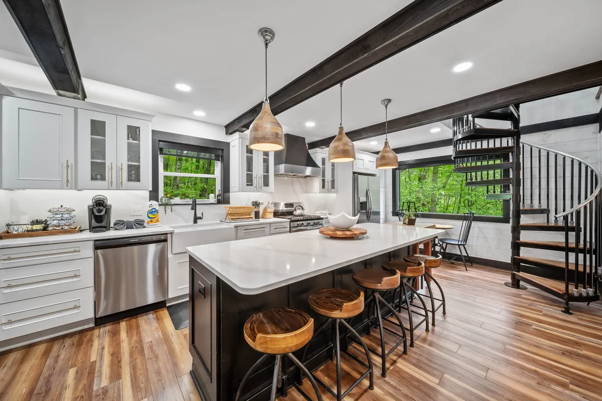 A modern, airy kitchen with a large island, spiral staircase, and contemporary appliances. Natural light floods the room from large windows, setting the stage for culinary adventures and social meals.