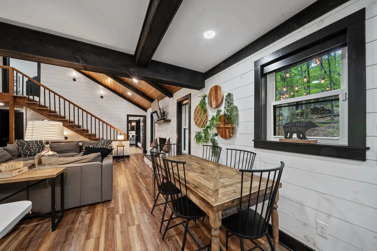 A warm dining area showcasing a large wooden dining table, surrounded by comfortable seating, adjacent to a window that frames lush greenery outside. The open plan allows for relaxed gatherings and scenic views during meals.