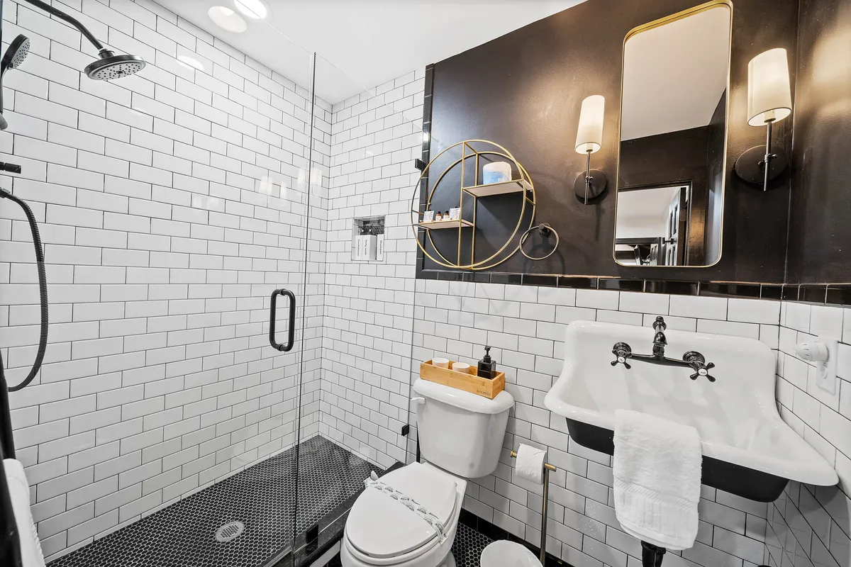 A contemporary bathroom with a glass shower enclosure, black accent wall, gold circular shelf, and white subway tiles. The space is inviting and sophisticated, offering a luxurious atmosphere for self-care routines.